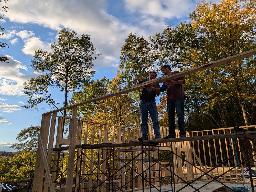 men working on raising a wall on a building in a woodsy area