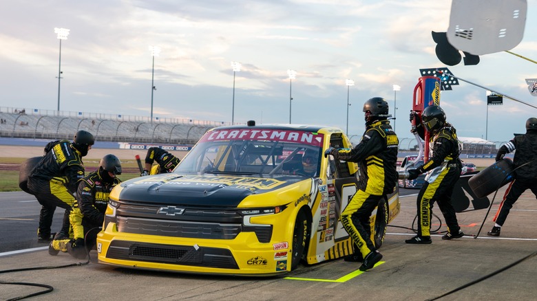 A pit crew works on a black and yellow NASCAR Truck Series truck in the middle of a race.