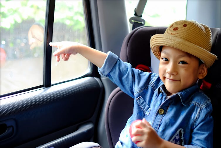 A young, smiling boy points out of a car window